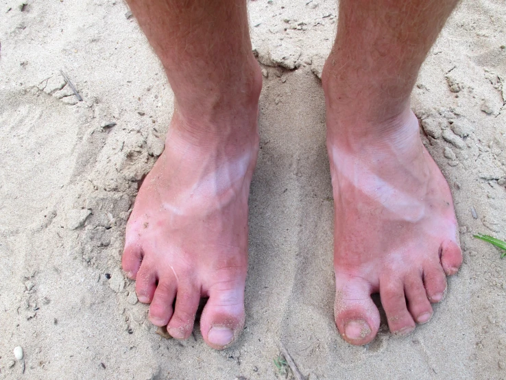 someone's bare feet standing in the sand with grass