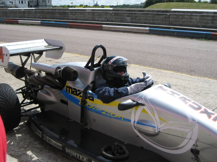 man in a silver and black race car driving down a street