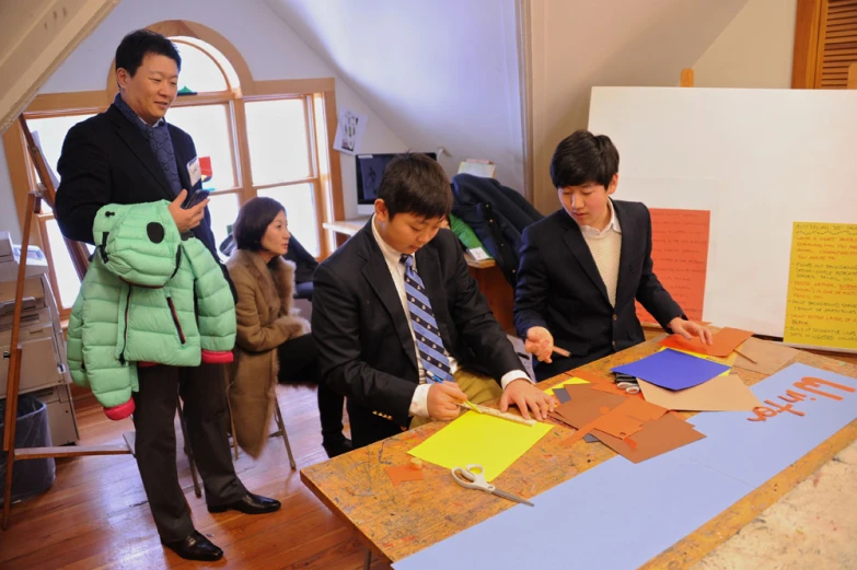 people in suits stand over a table while looking at signs