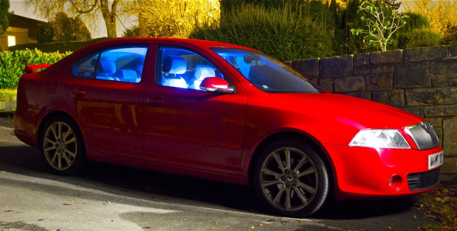 red car parked in residential neighborhood next to tall brick wall