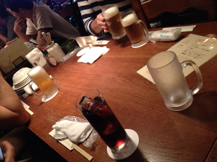 people drinking beer at a wooden table with white napkins and papers