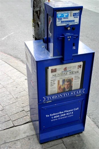 a newspaper dispenser sitting on the sidewalk on the corner of a city street
