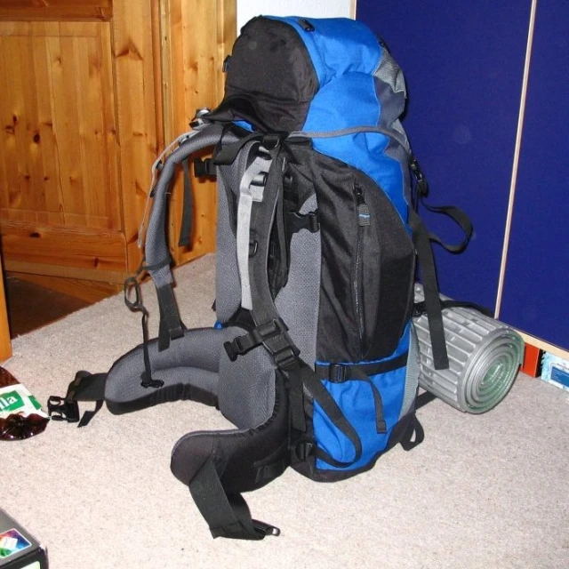 a blue and grey backpack sitting on the floor next to a wall