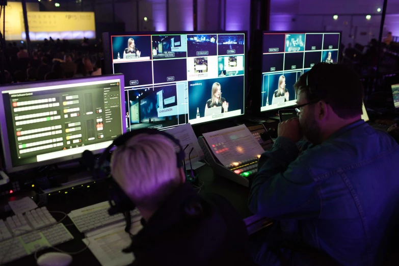 two people sitting at a table with multiple computer monitors in front of them