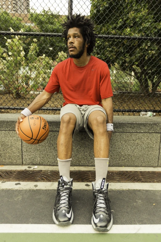 a person in red shirt sitting on cement bench holding a basketball