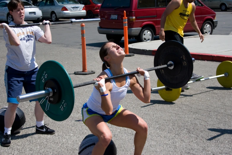 a woman lifting barbells while another man holds his hands