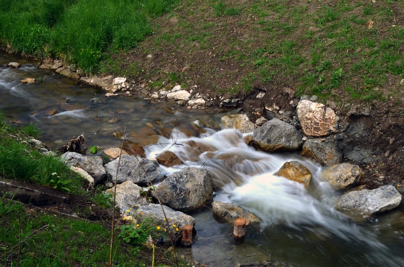 a stream of water surrounded by rocks and green grass