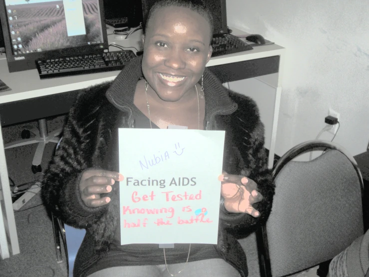 a woman sitting down with a sign reading facing aids get tested currently 2 % out of 1 % the grade