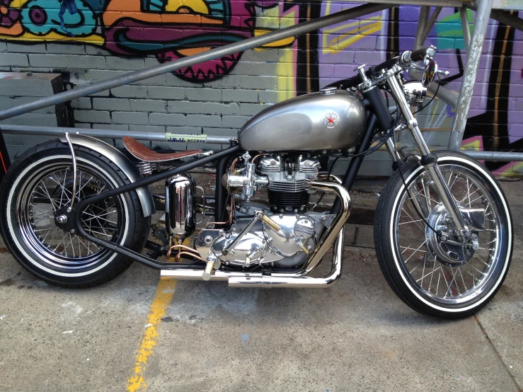 an old - fashioned motorcycle with chrome parts parked in front of graffiti