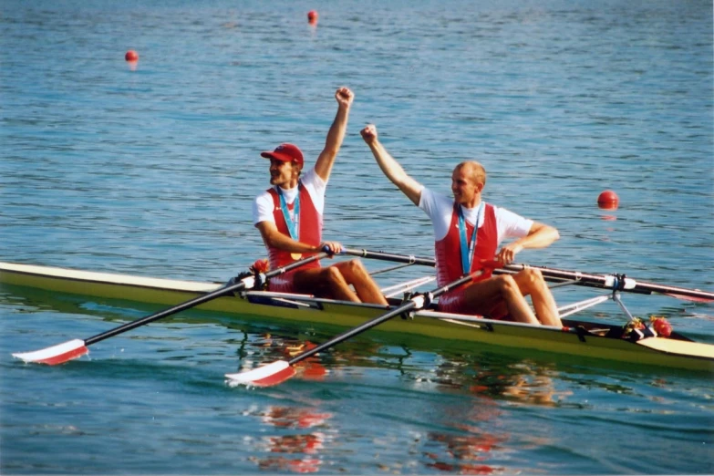 two people on a boat in the water with their arms raised