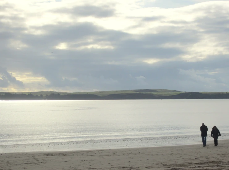 two people stand on the shore with a dog