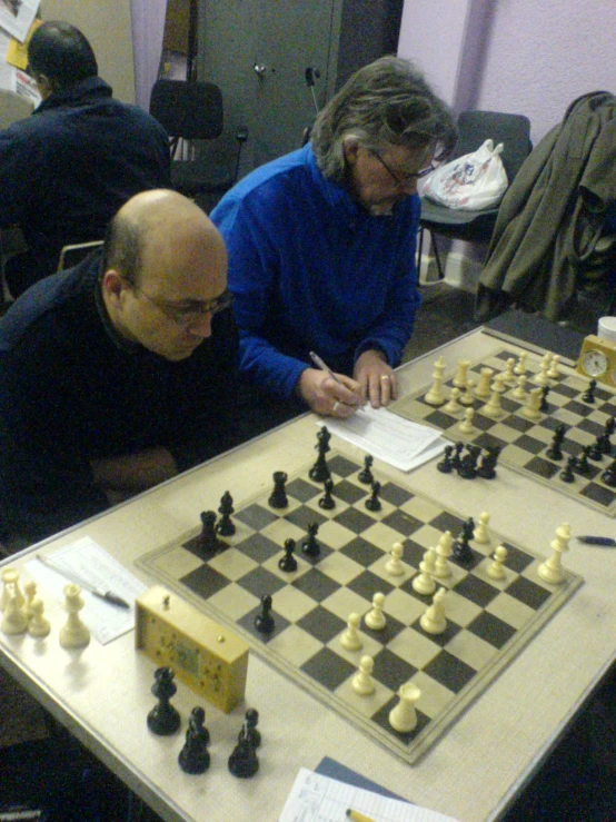 two older men play chess on a long table