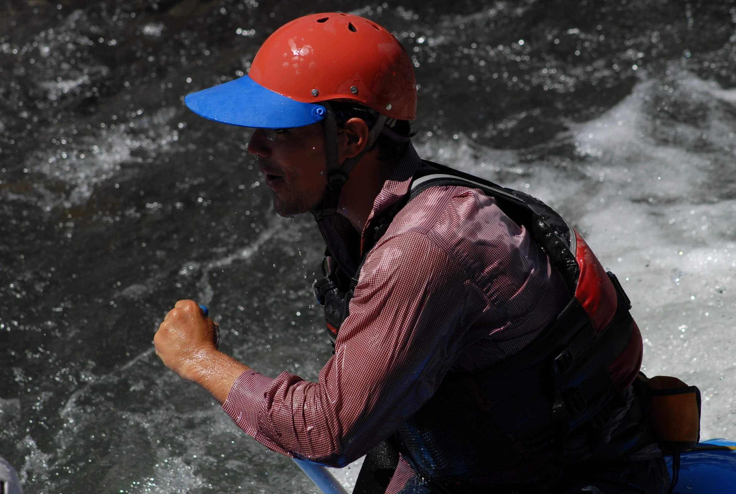 man in a red helmet and blue life jacket white water rafting