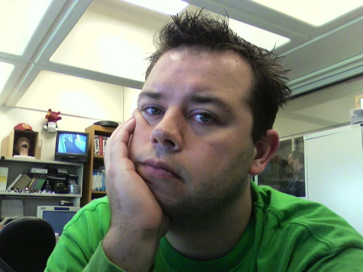 a man wearing a green shirt sits in front of a computer