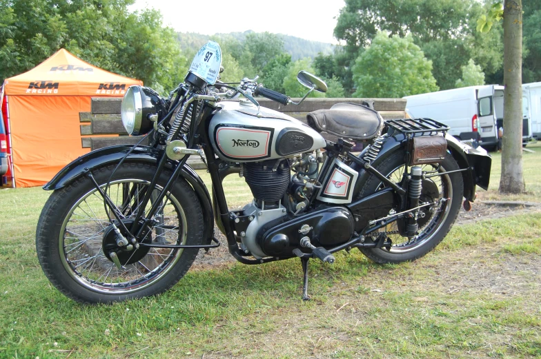 the old black motorcycle is parked under a tree