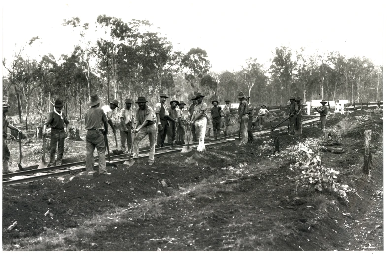 men are on a railroad track holding poles and walking in the dirt