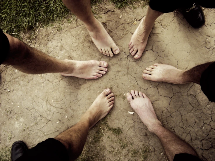 four bare feet on the ground surrounded by grass