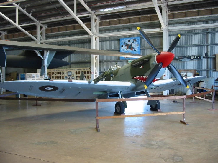 a blue plane in a garage with another airplane on the ground