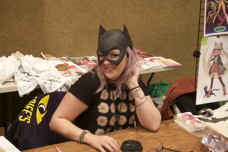 a woman with pink hair and cat mask sitting at a table