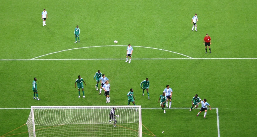 many players stand on a soccer field as a ball comes toward them