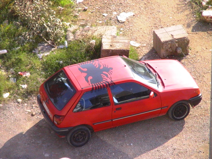 a red car parked near a trail with an animal decal on it