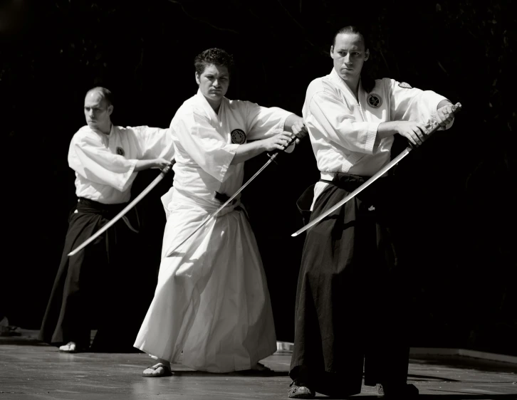 three men in a black and white po standing with swords