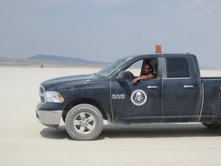 a woman driving a black truck on a beach