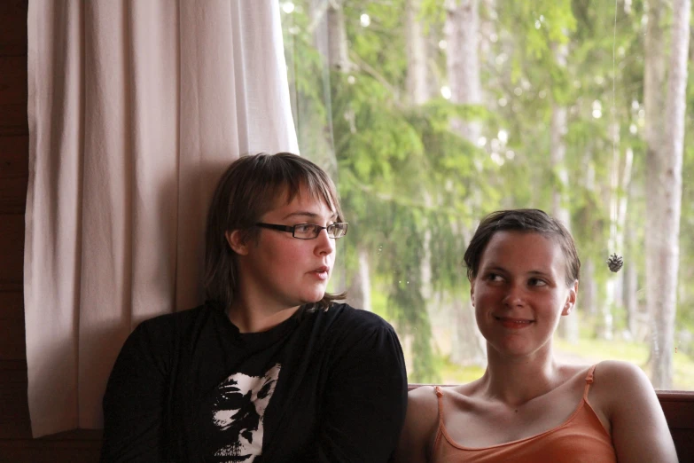 two women sitting on the side of a wooden bench