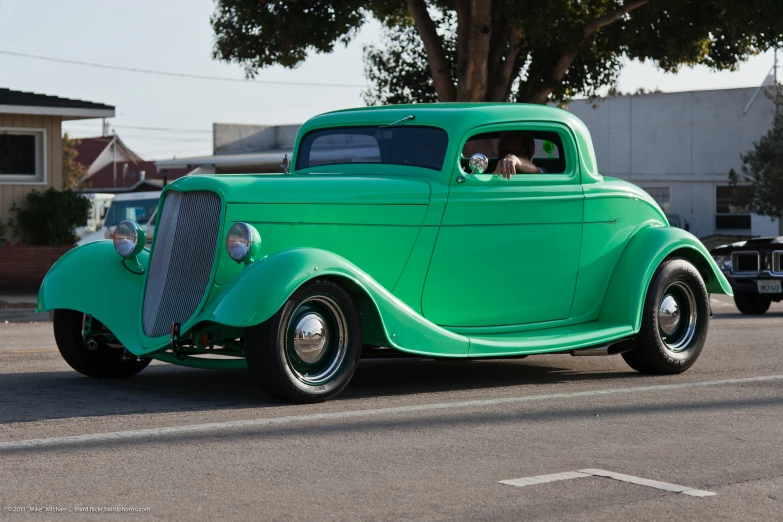 an old green classic car is driving down the street