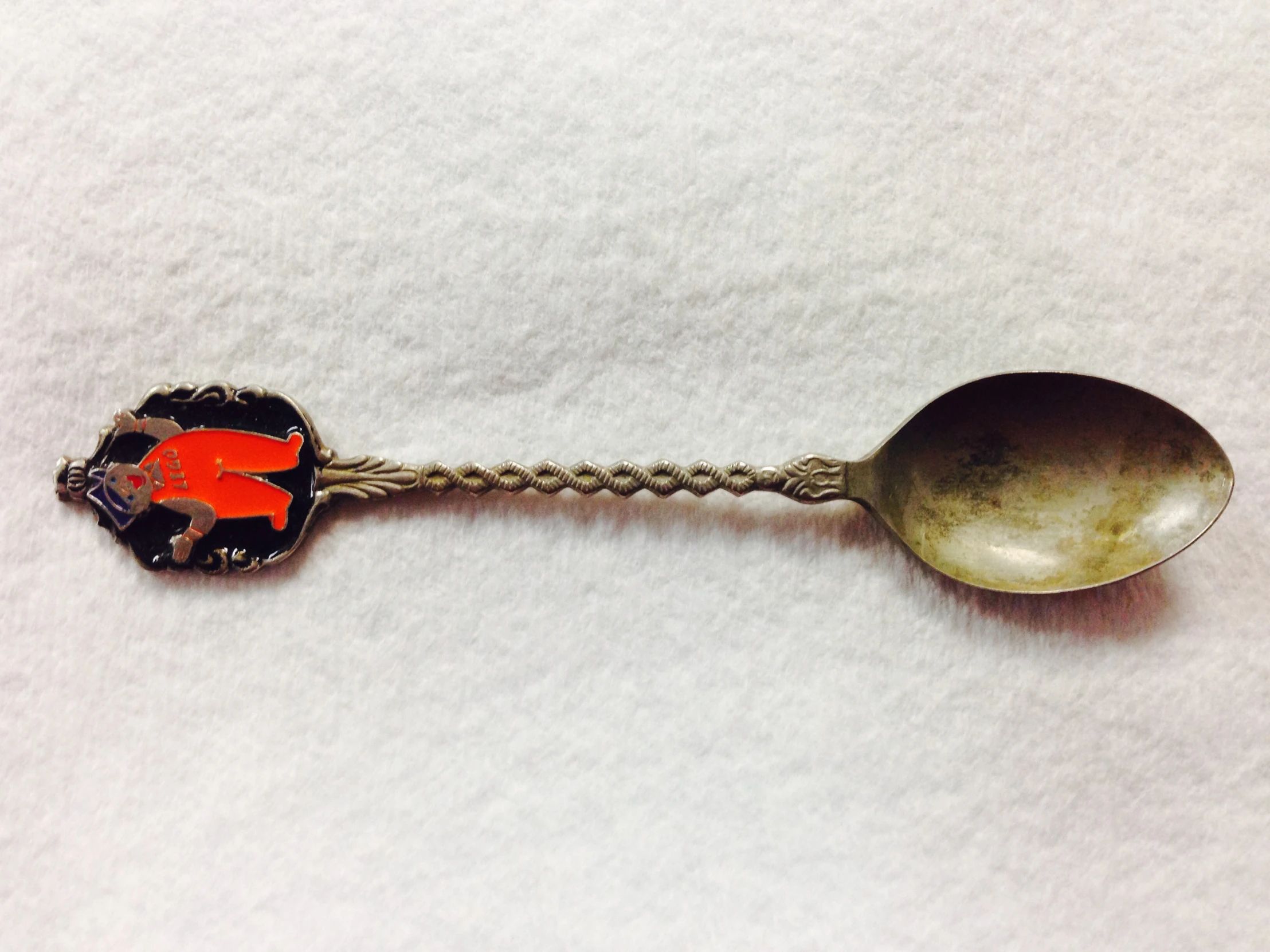 a spoon and a spoon shaped brooche with an orange person on it