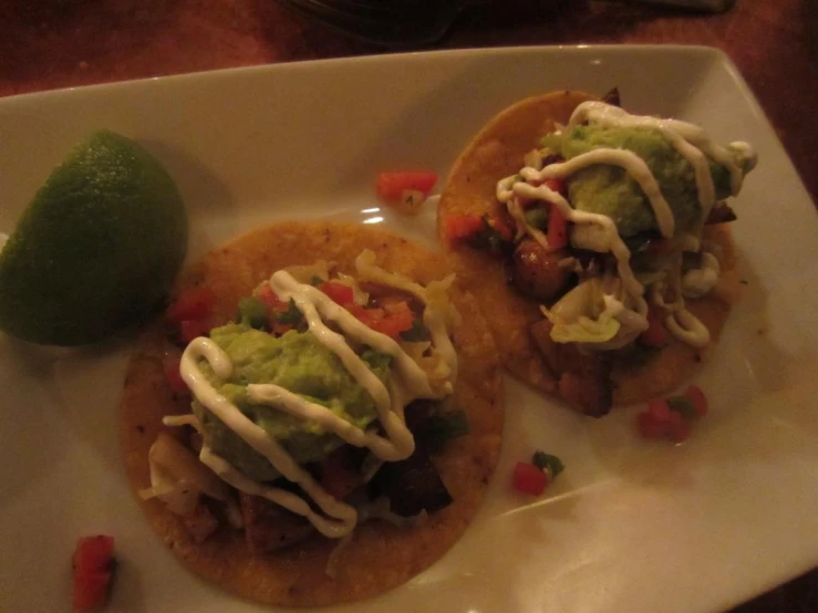 two tacos sit on a plate with a lime and a tortilla