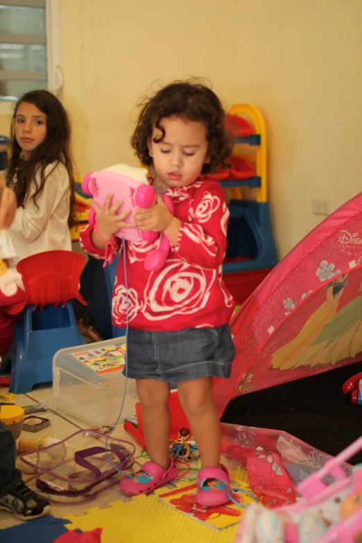 a girl in a red shirt is standing in a room with a pink umbrella