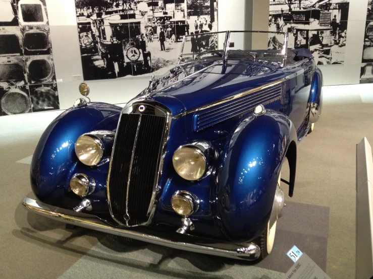 a vintage car sitting in a museum with some pictures on the walls