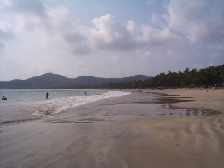 three people walking along a sandy shore next to the ocean