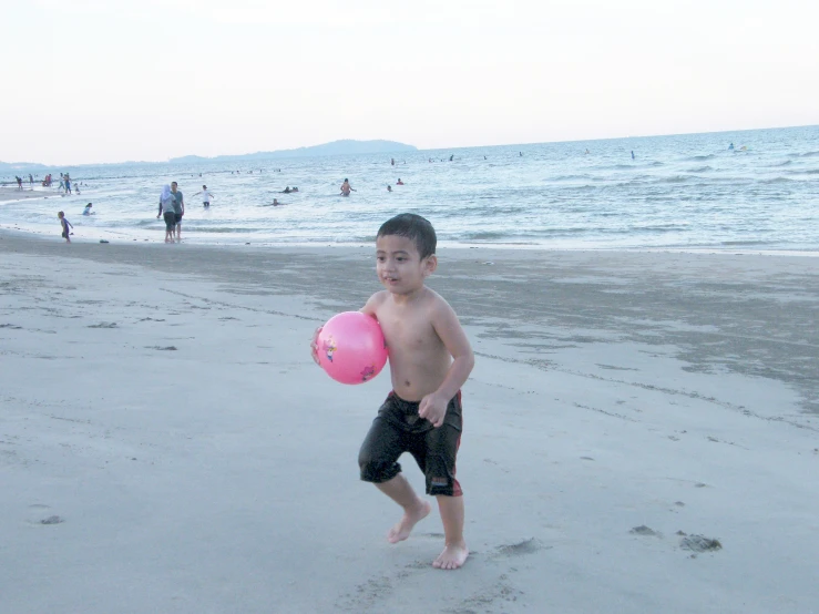 a boy walking on the beach with his ball