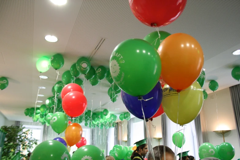 people gathered under a room full of green and red balloons