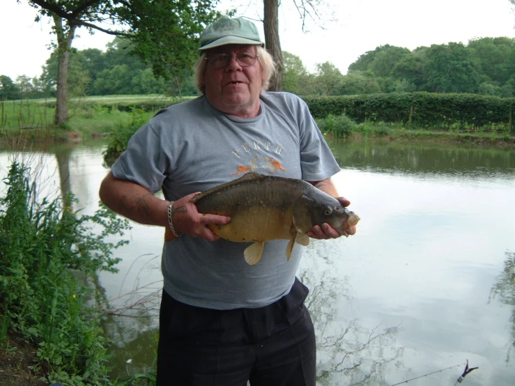 an older man holding a fish next to some water