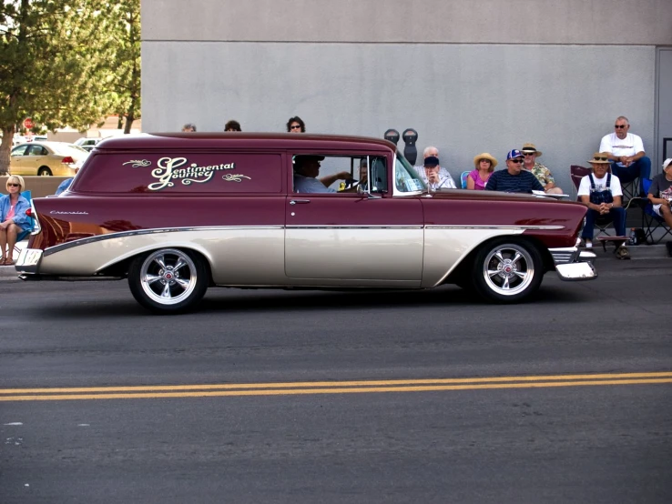 a maroon and gold vintage car driving down the street