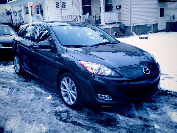 a black mazda car parked in front of two houses