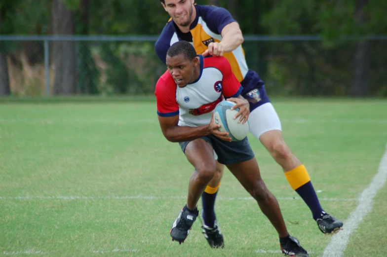 two rugby players on opposing teams with one trying to control the ball