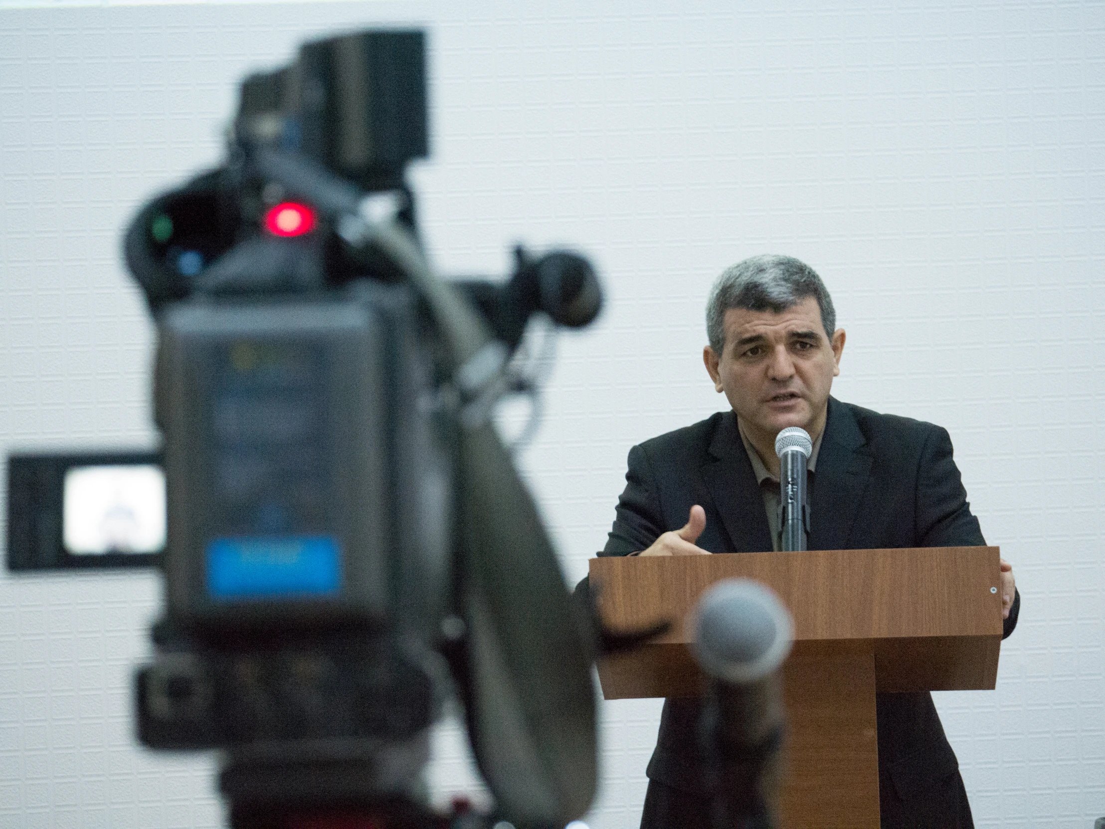 a man speaking while behind a podium with camera