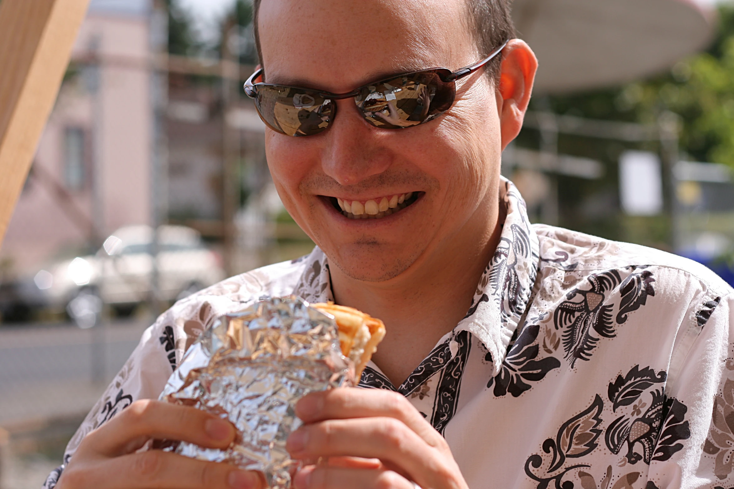 man smiling while eating a pastry item outside