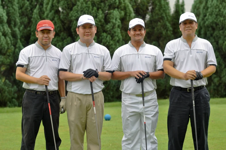 five men standing on a grass covered field with their golf bats
