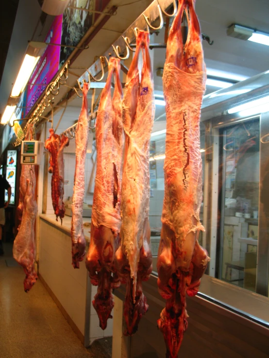 meat hanging in a store with a person standing behind them
