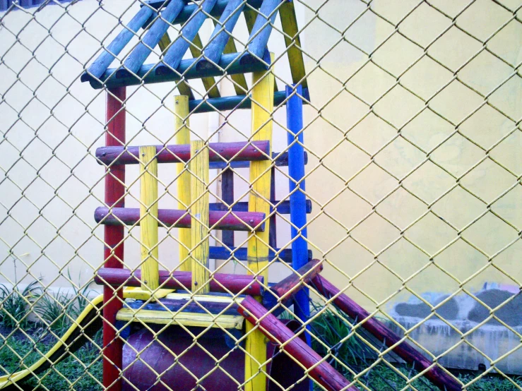 a colorful wooden child's play set in the grass behind a fence