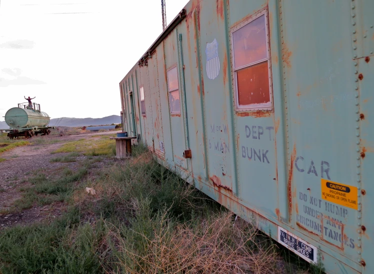 a green train car sitting in a field with graffiti on it