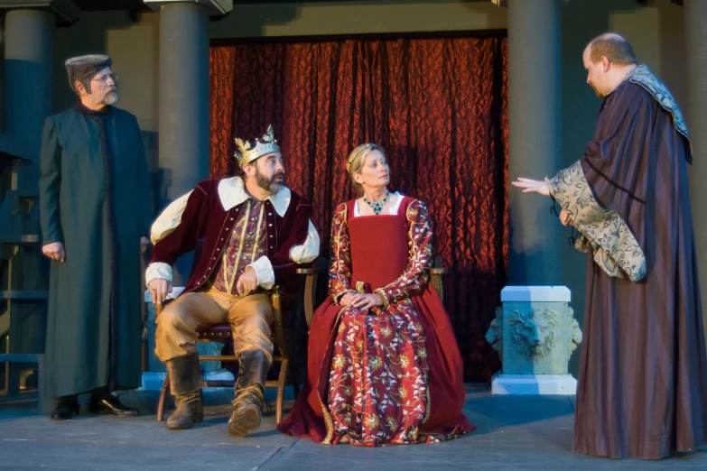 three people in renaissance costumes talking and seated on stage