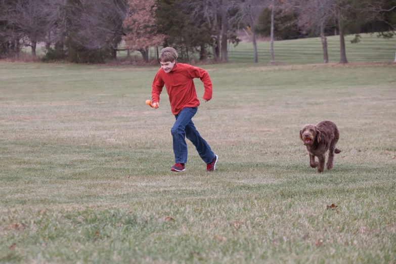 the young person in a red shirt is running with a brown dog