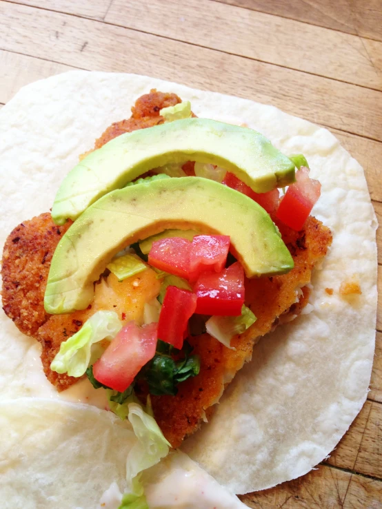 a tortilla with avocado, tomatoes, cucumber and lettuce on it