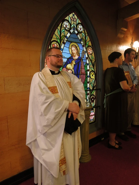 priest standing in front of stained glass window in church